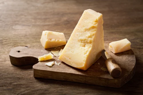 Na imagem, há um pedaço de queijo parmesão em tábua de madeira