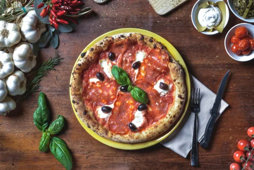 Na imagem, há uma pizza napolitana com molho de tomate, queijo e manjericão
