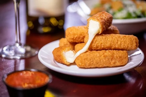 Na imagem, há diversos palitos de queijo mussarela em prato branco