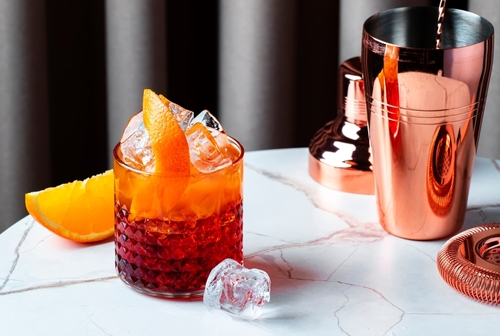 Na imagem, há um copo do drink italiano Negroni em cima da mesa