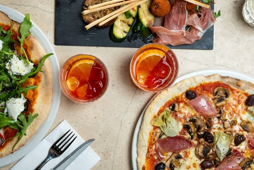 Na imagem, há uma mesa com pizza e dois copos de drinks